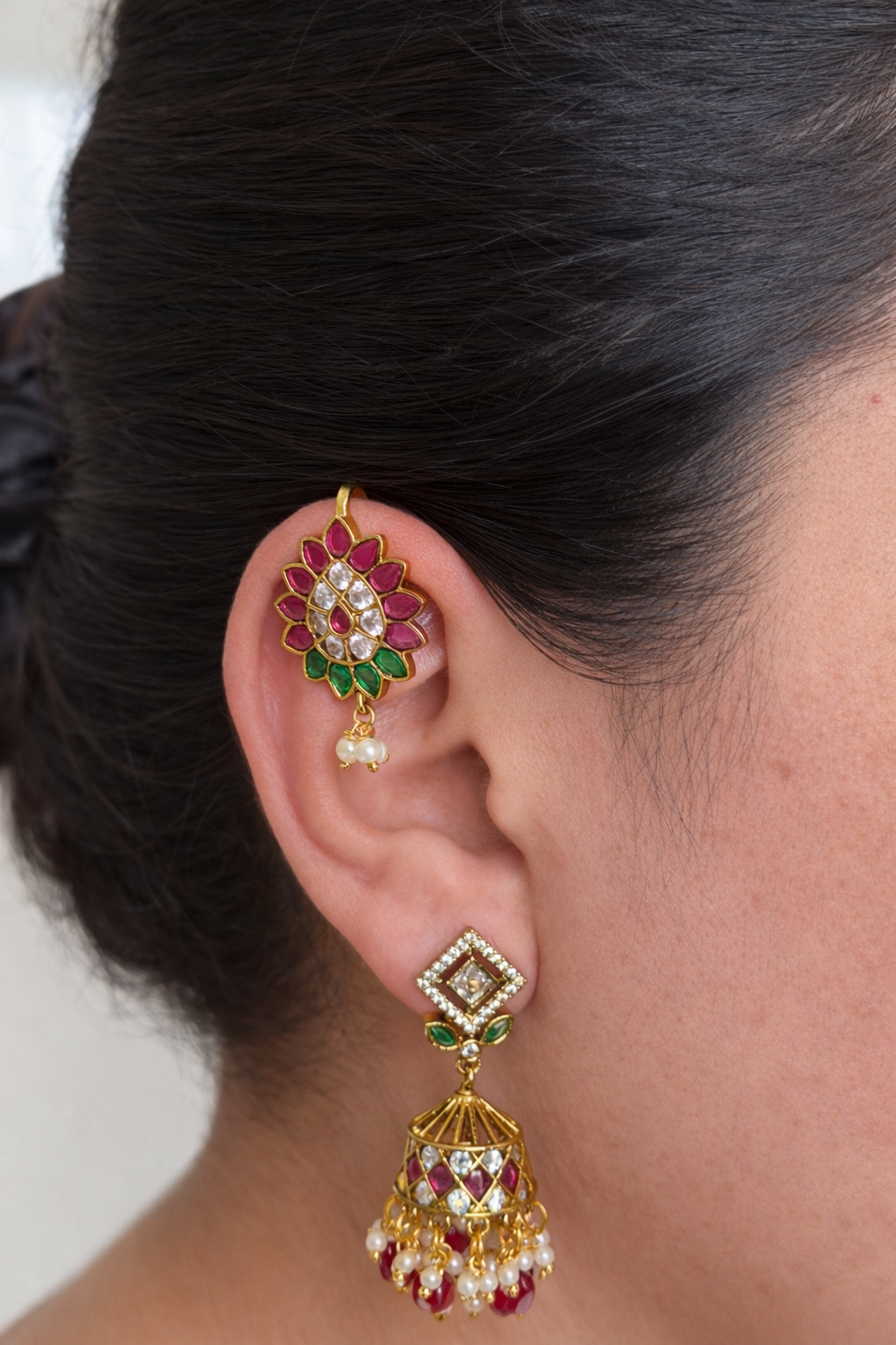 Close-up of an ear with bugdi and gemstone earrings against a neutral background