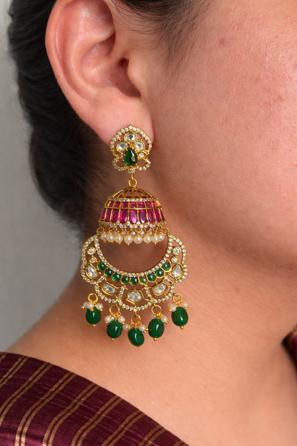 Close-up of a person wearing a gold look alike earring with green and red stones.