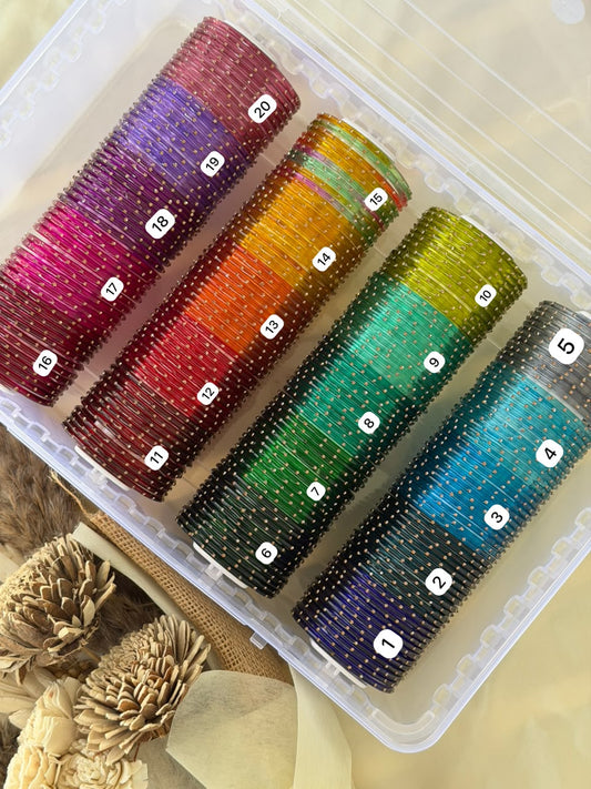 A clear plastic organizer containing four large rolls of small round beads in different colors, each roll labeled with a number. The beads show a striped pattern of metallic gold and translucent shades of pink, red, orange, green, blue, and purple.