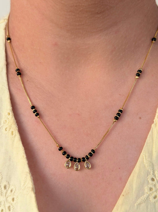 Necklace with black beads and gold accents on a person wearing a yellow top.