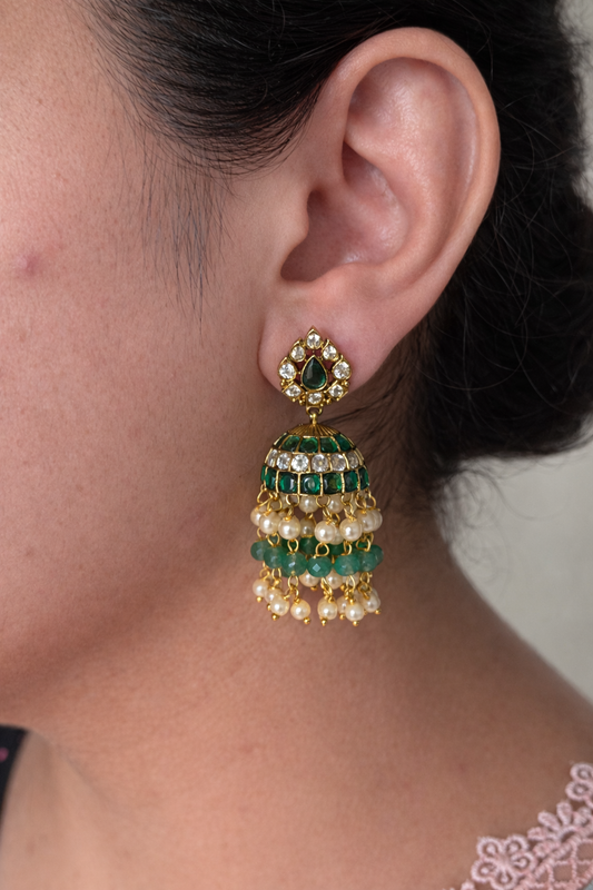 Close-up of an ear wearing a green kemp gold look alike earring with a blurred background