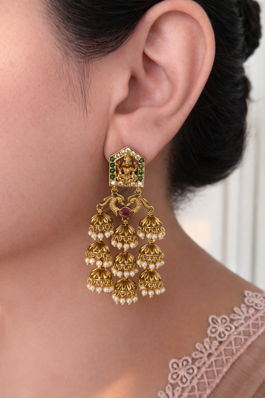 lakshmi devi earrings with green gemstones and pearl drops worn by a person.