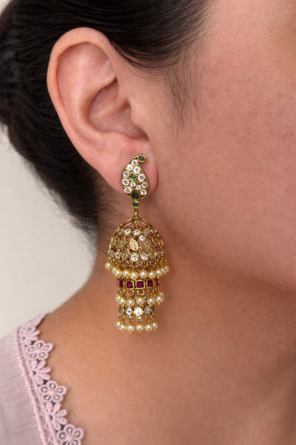 Close-up of a person wearing a multi jhumka earrings and red earring with green gemstones.