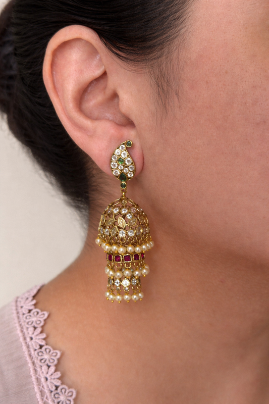 Close-up of a person wearing a multi jhumka earrings and red earring with green gemstones.