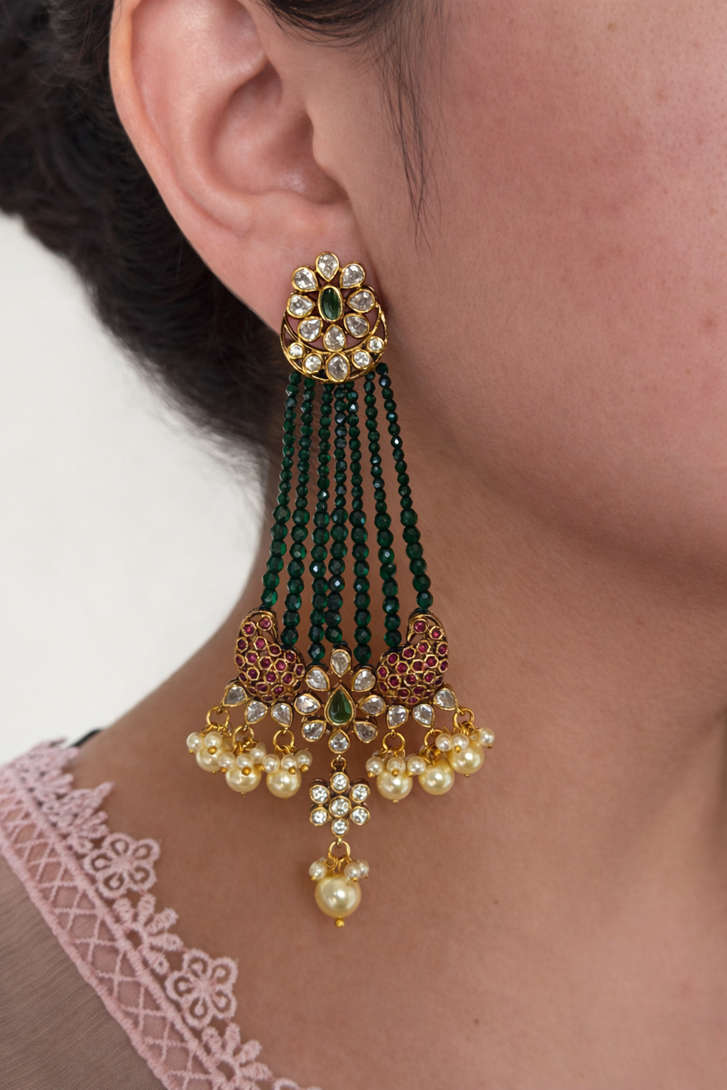 Close-up of a person wearing a pair of ornate earrings with green and gold details.