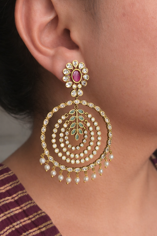 Ornate gold look earring with pearls and gemstones worn by a person.