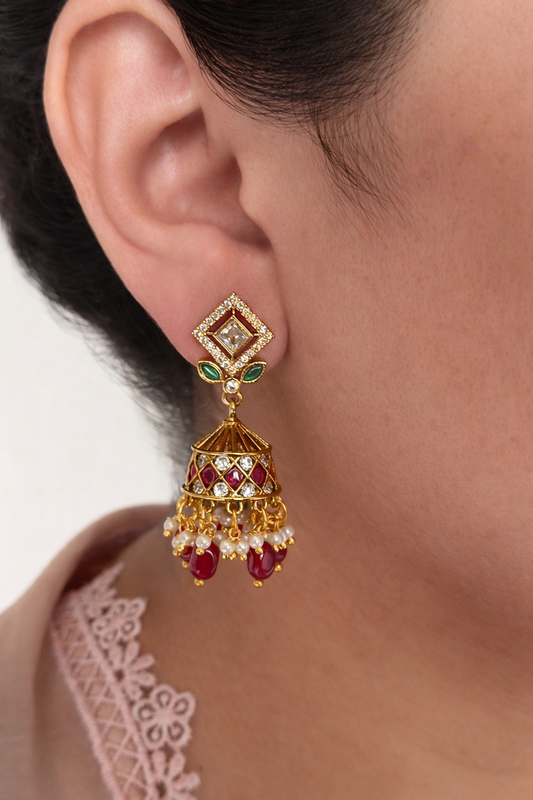 Close-up of a person wearing a gold and red gemstone earring.