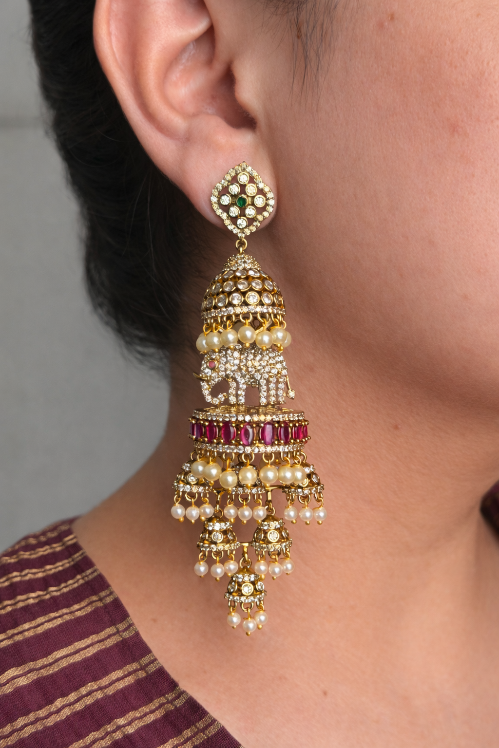Gold and pearl earring with red stones worn by a person against a neutral background