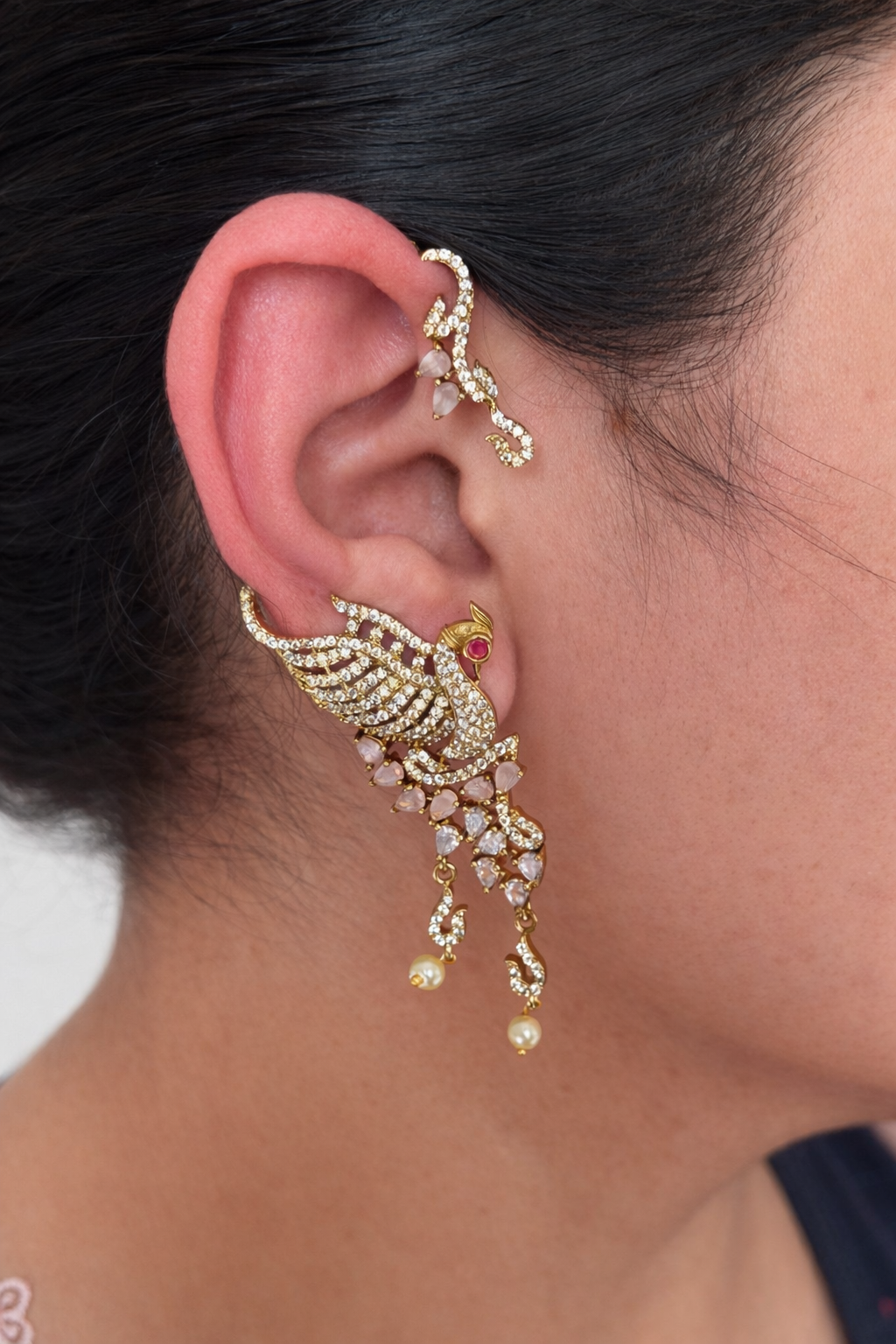 Close-up of an ornate gold look alike earcuff earring with a red gemstone worn by a person.